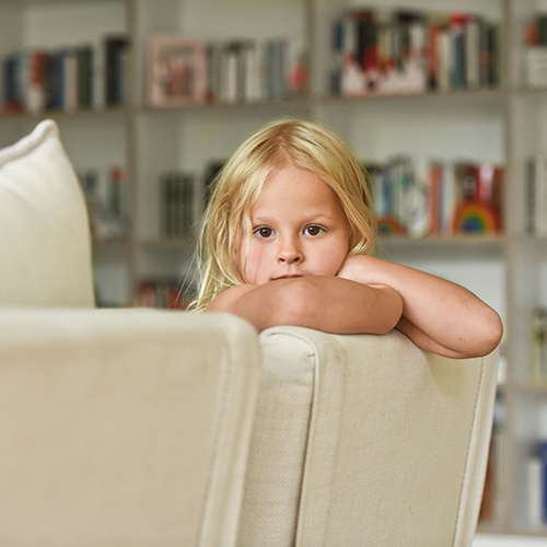 Kleines Mädchen sitzt auf einem cremefarbenen Sofa und schaut über die Rückenlehne