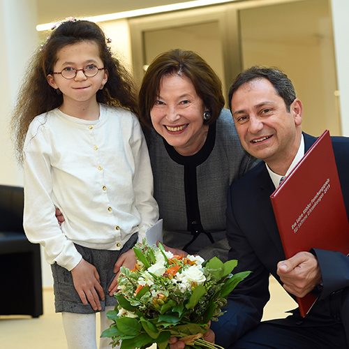 Eva Luise Köhler schaut gemeinsam mit dem Forschungspreisträger 2015 und einem betroffenen Mädchen in die Kamera.
